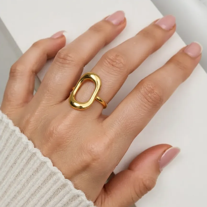 Hand wearing a gold ring on a neutral background