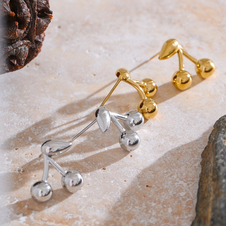 Gold and silver cherry-shaped waterproof earrings on a textured surface