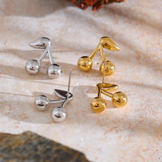 Gold and silver cherry-shaped earrings on a textured surface