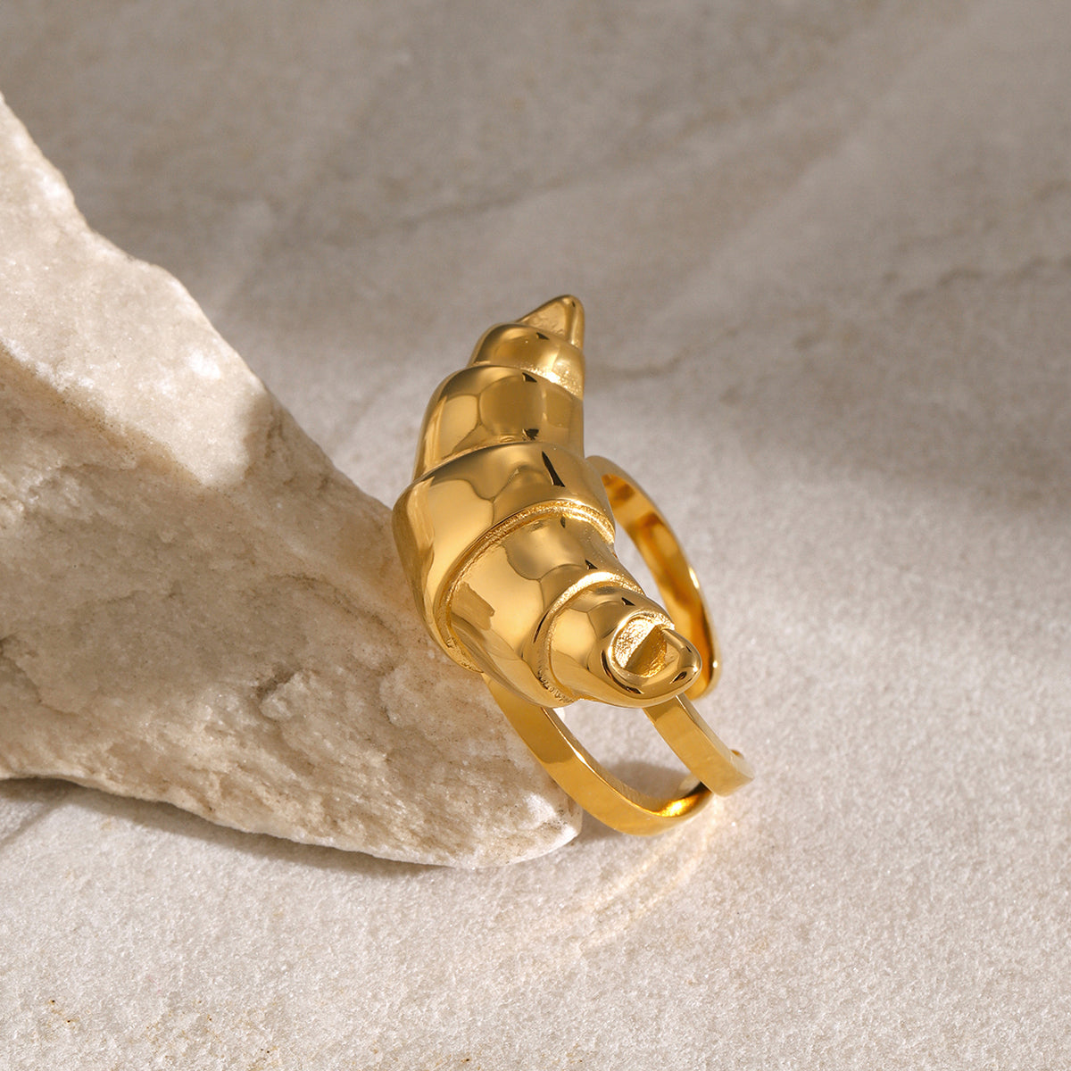 Gold stainless steel in a shape of a croissant on a beige stone surface