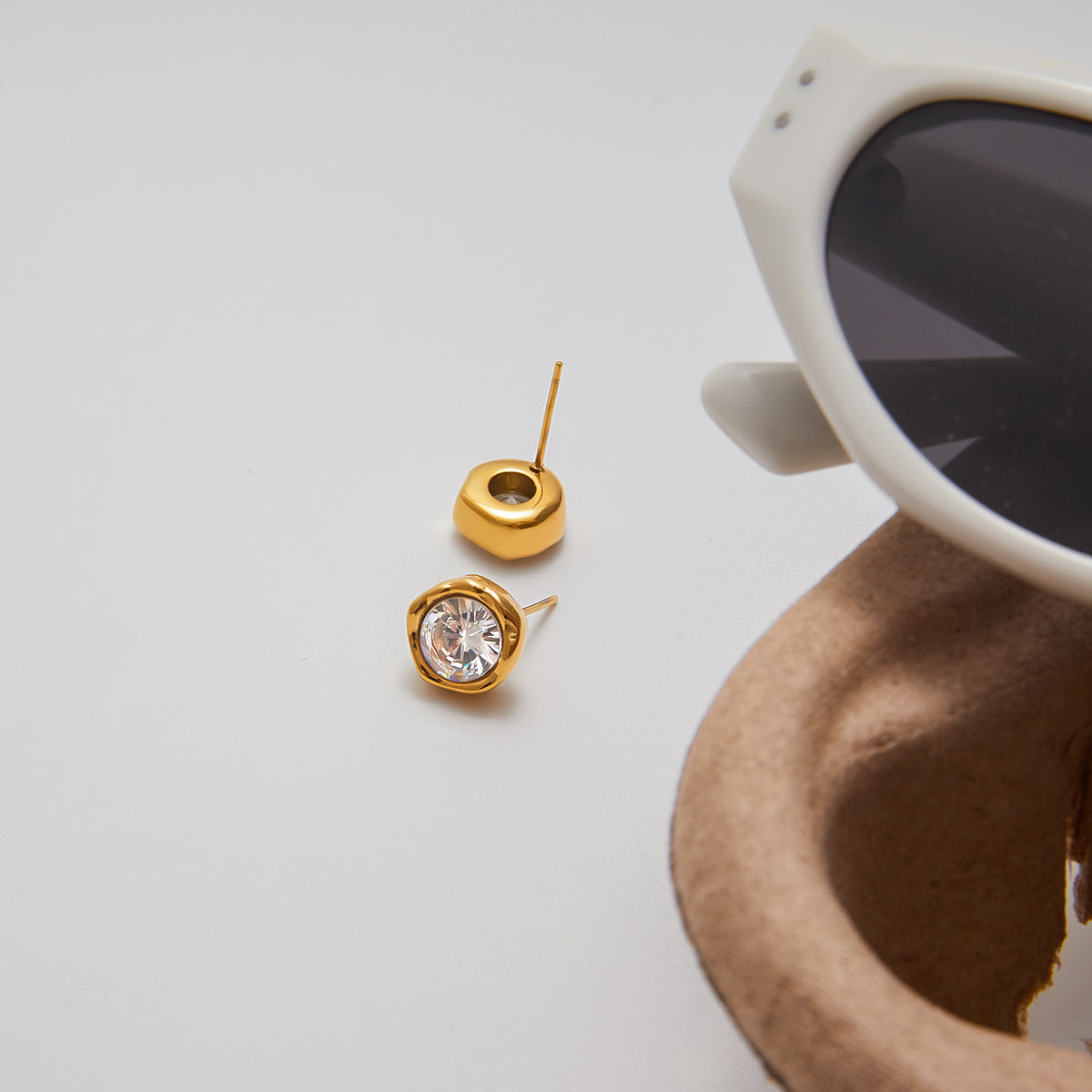 Gold earrings with a clear gemstone on a light gray background