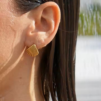 Close-up of an ear wearing a gold stainless steel earring with a blurred natural background