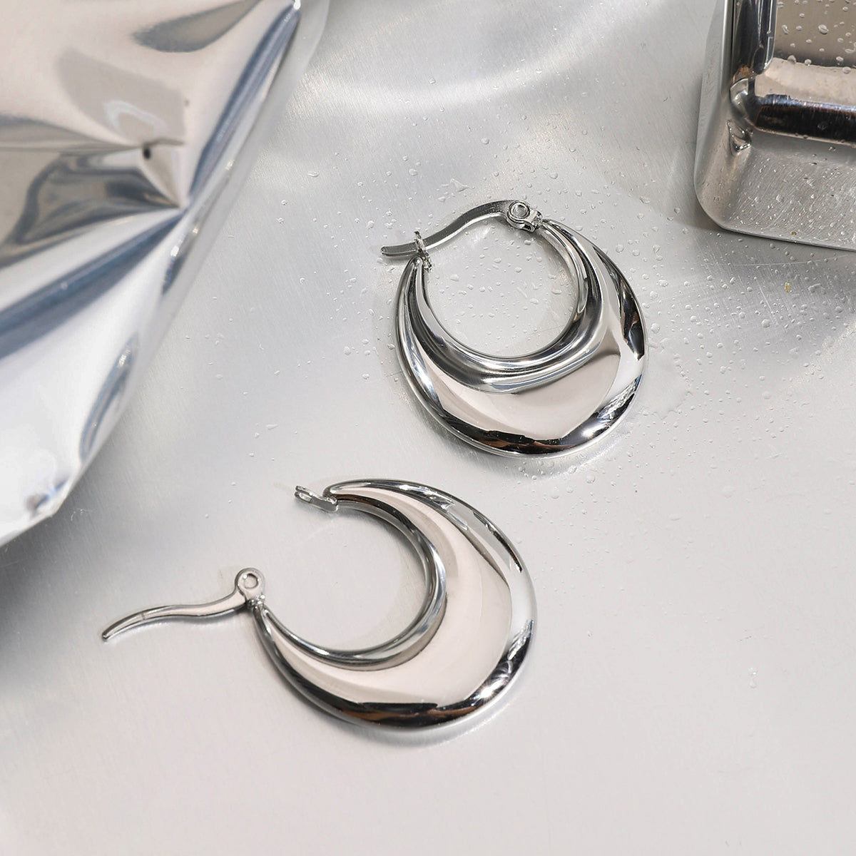 Silver stainless steel hoop earrings on a reflective surface