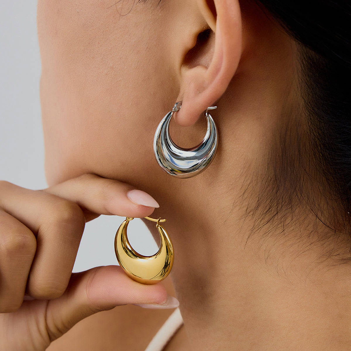 Close-up of a person wearing gold and silver hoop earrings with one hand holding a gold hoop earring.