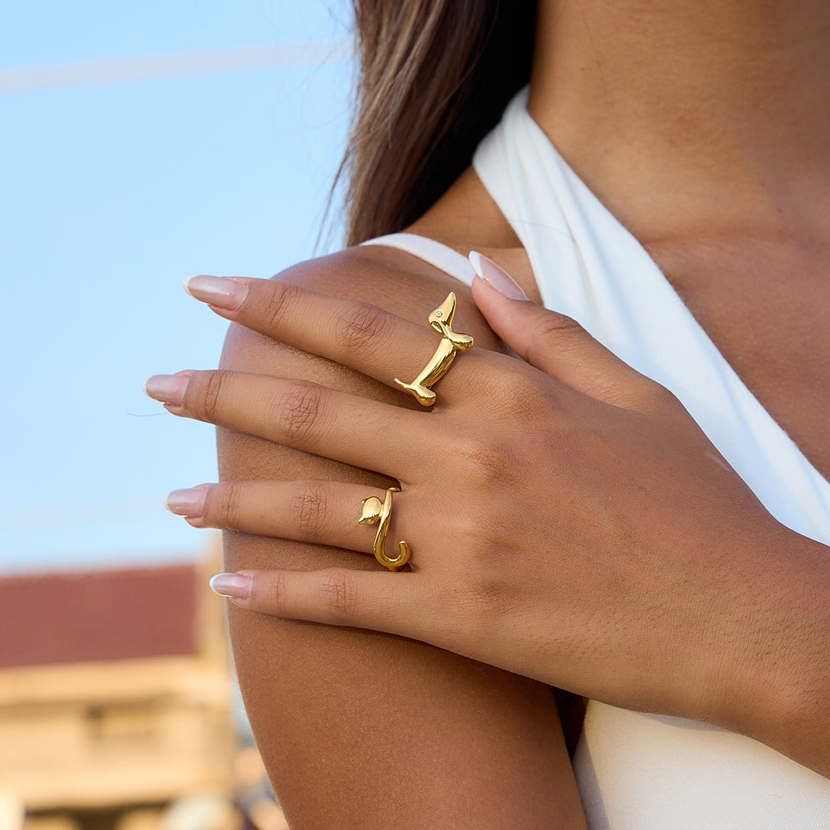Close-up of a person wearing two gold rings on a blurred outdoor background