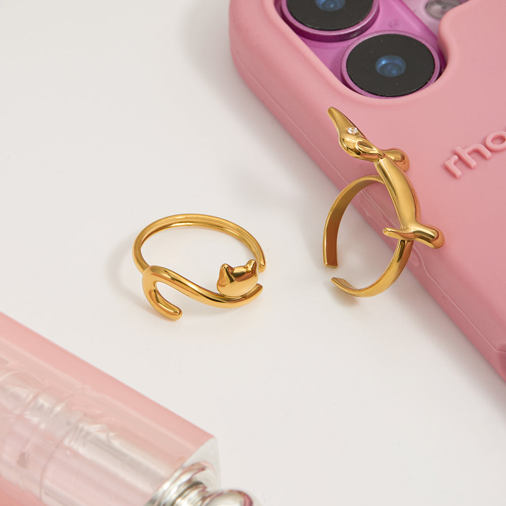 Gold cat-shaped ring on a white surface with a pink phone case in the background.
