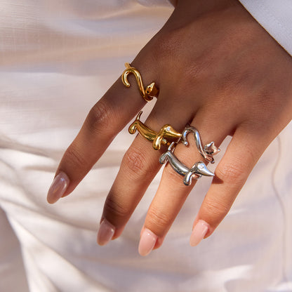 Hand wearing gold and silver cat-shaped rings on a neutral background