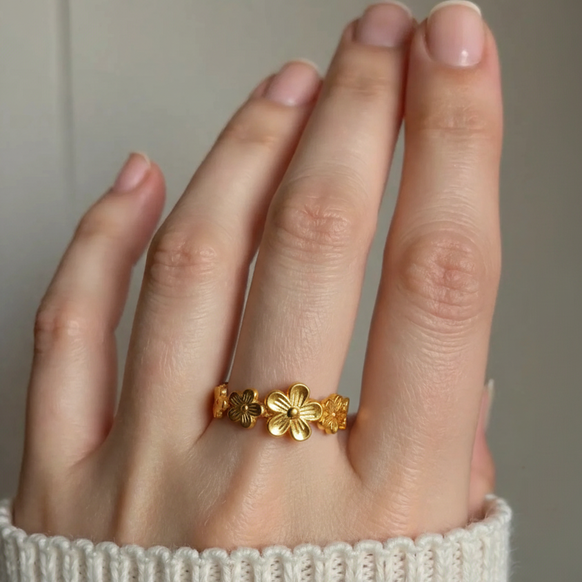 Gold floral ring on a person's finger with a neutral background