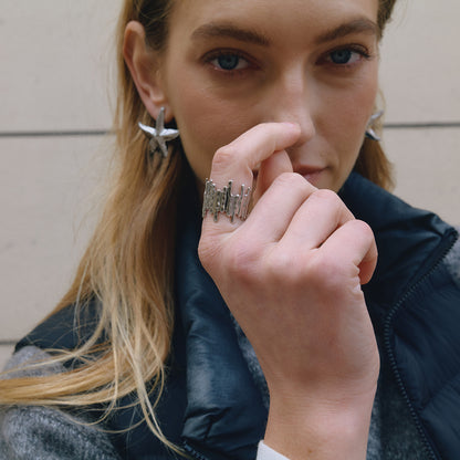 Close-up of a person wearing earrings and a ring, with a neutral background