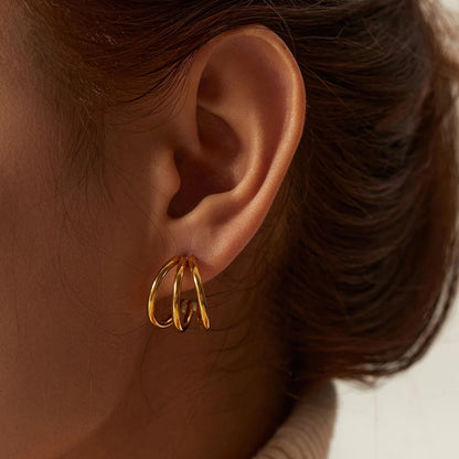 Close-up of an ear wearing a gold stainless steel hoop earring with blurred hair and background