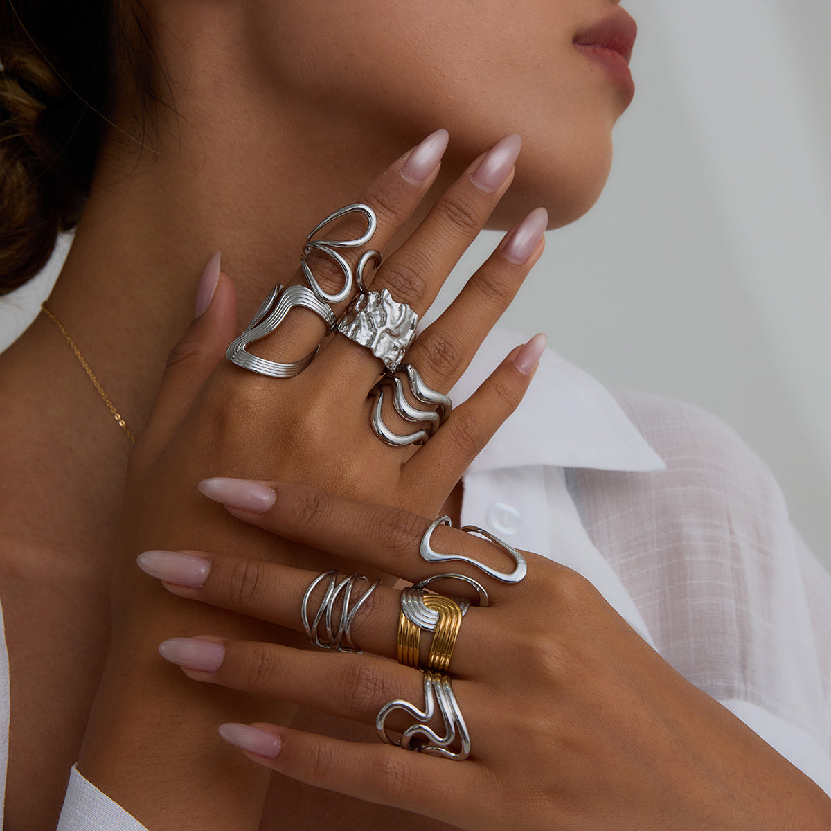 Close-up of a hand wearing multiple silver rings with a neutral background