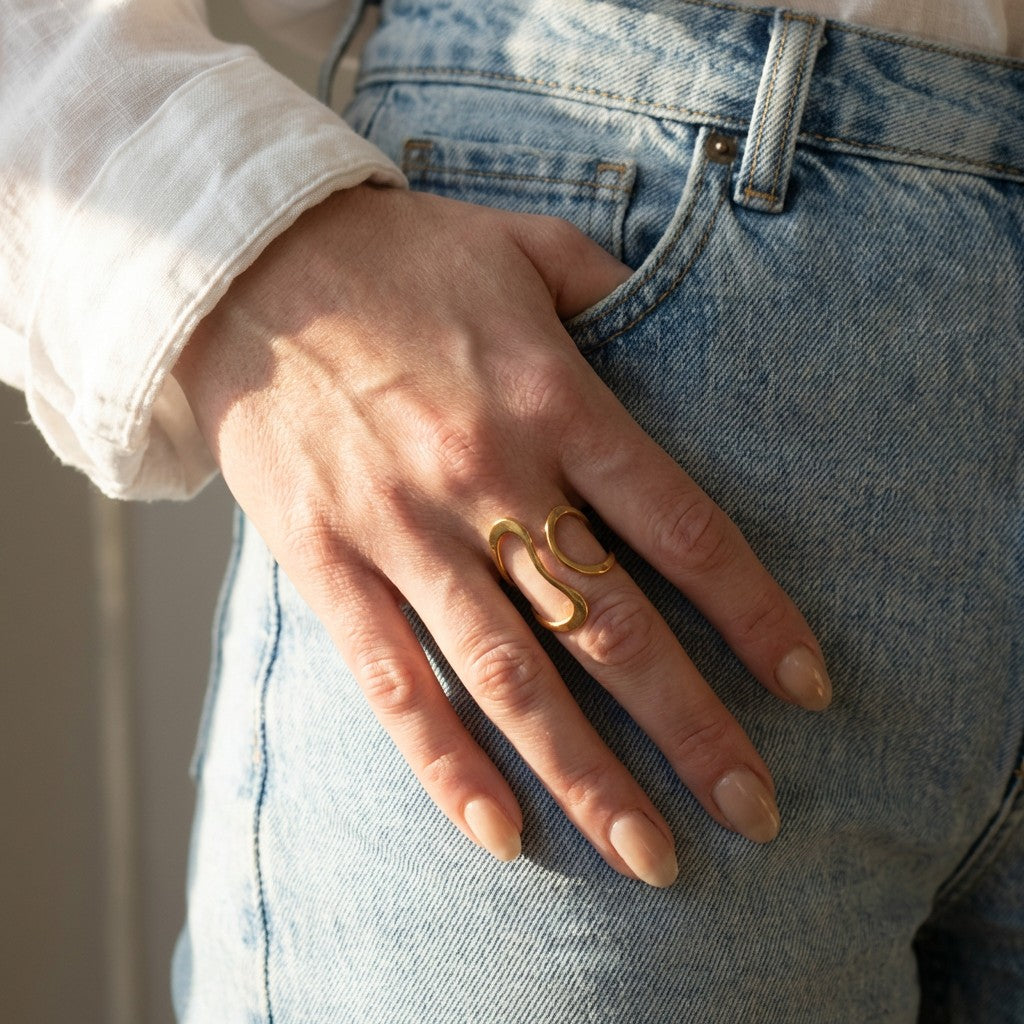 Hand wearing an elegant gold ring with a 'C' design on a denim background