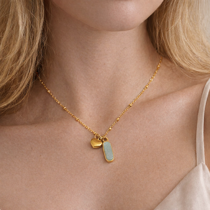 Gold necklace with two pendants on a person wearing a beige top.