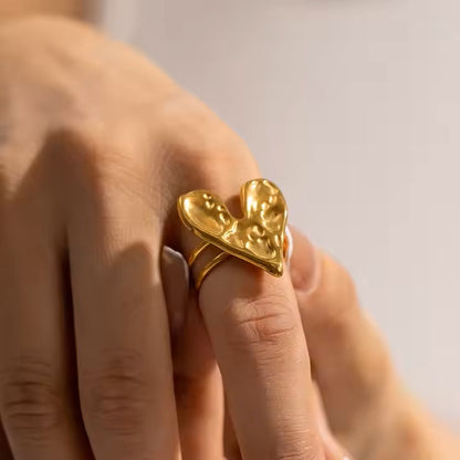 Gold heart-shaped ring on a person's finger with a blurred background
