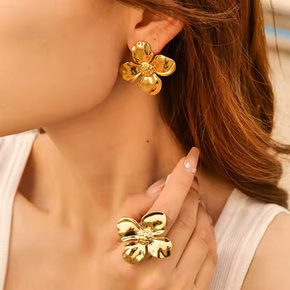 Close-up of a person wearing stainless steel gold flower earrings and a matching ring.