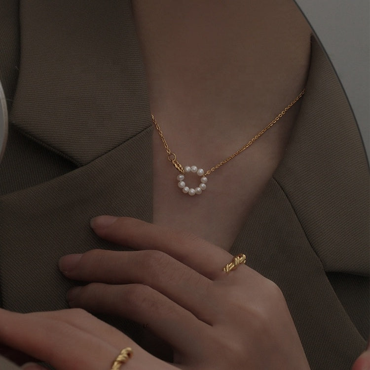 Close-up of a person wearing a gold necklace with pearl-like beads and matching rings on a dark background.