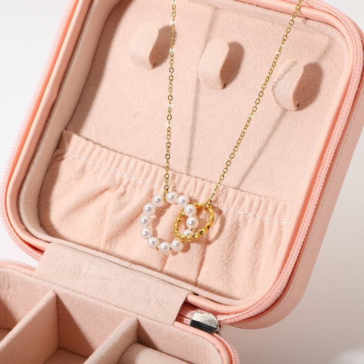 Gold necklace with a circular pendant and pearl beads in a pink jewelry case.