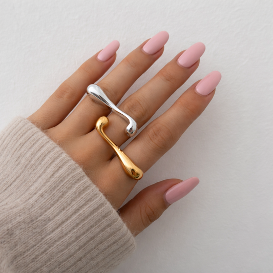 Hand wearing two rings with pink nail polish on a neutral background