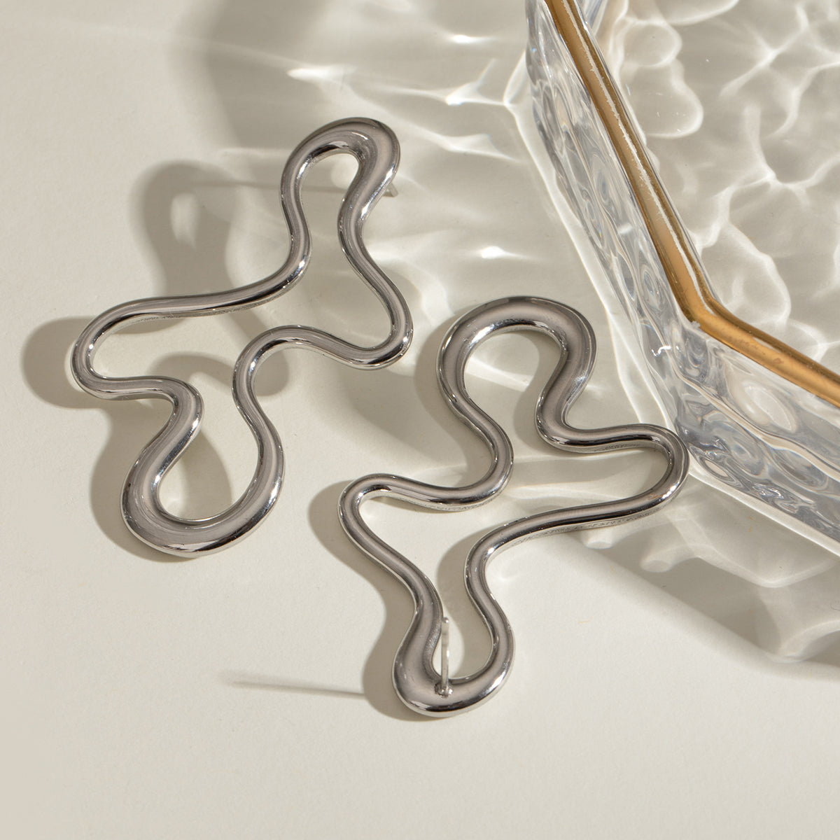 Silver stainless steel wavy earrings on a reflective surface