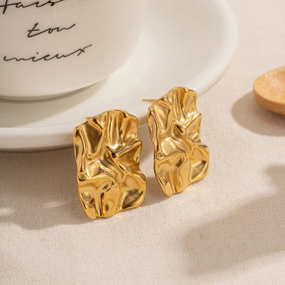 Gold earrings on a beige surface with a white dish in the background