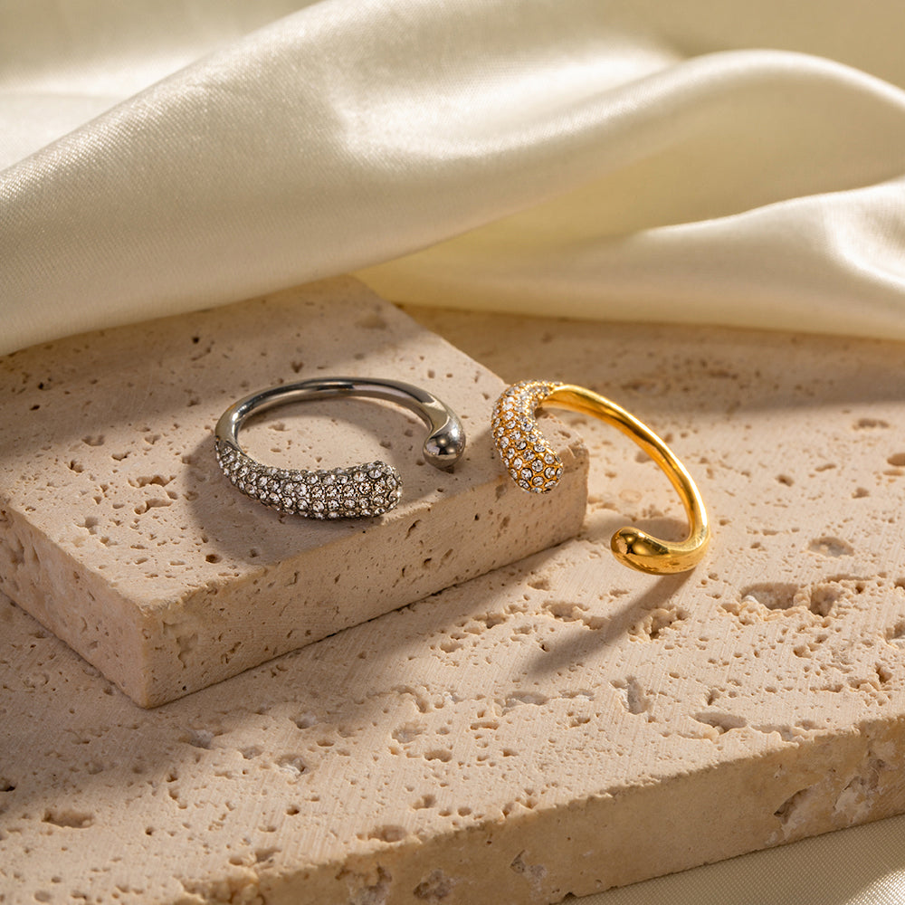 Two rings, one silver and one gold, on a textured stone surface with a soft fabric background.