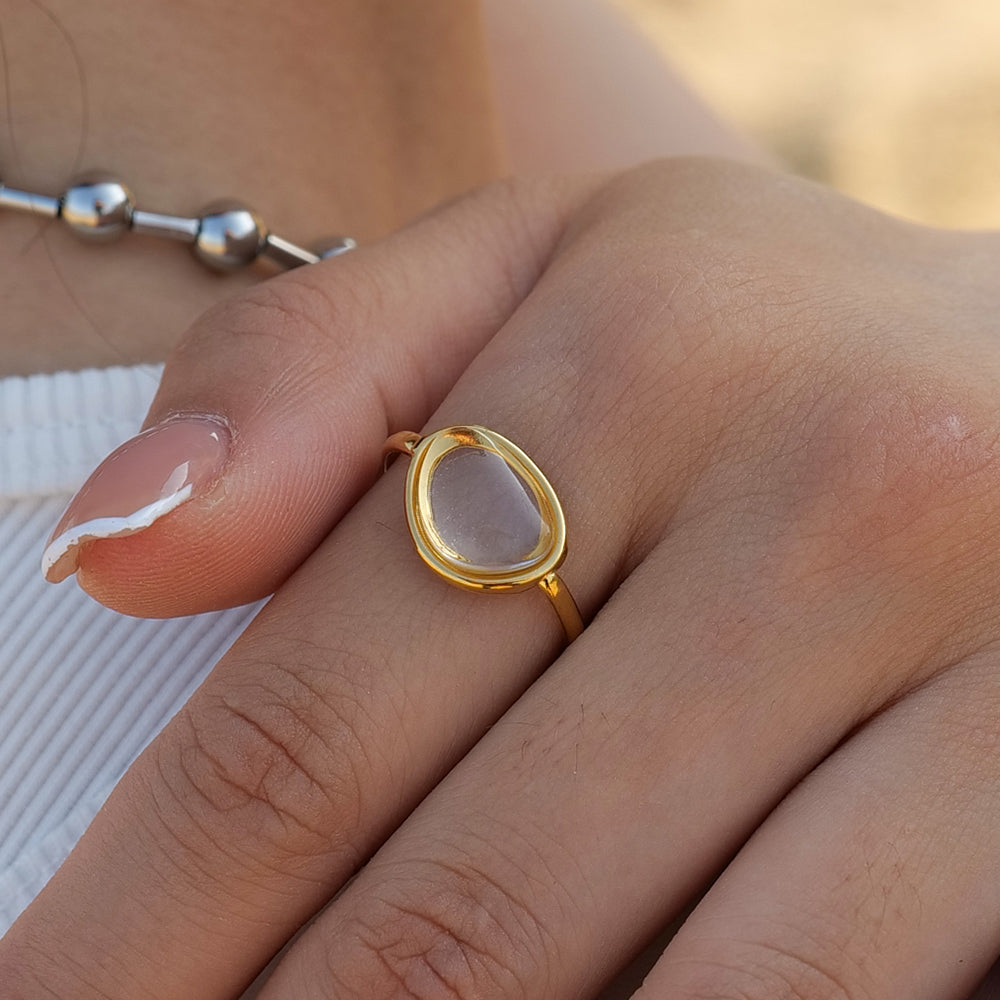 Gold waterproof ring with a pink stone on a person's finger