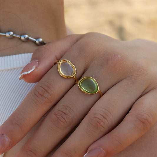 Close-up of a hand wearing two gold rings with green and clear gemstones.