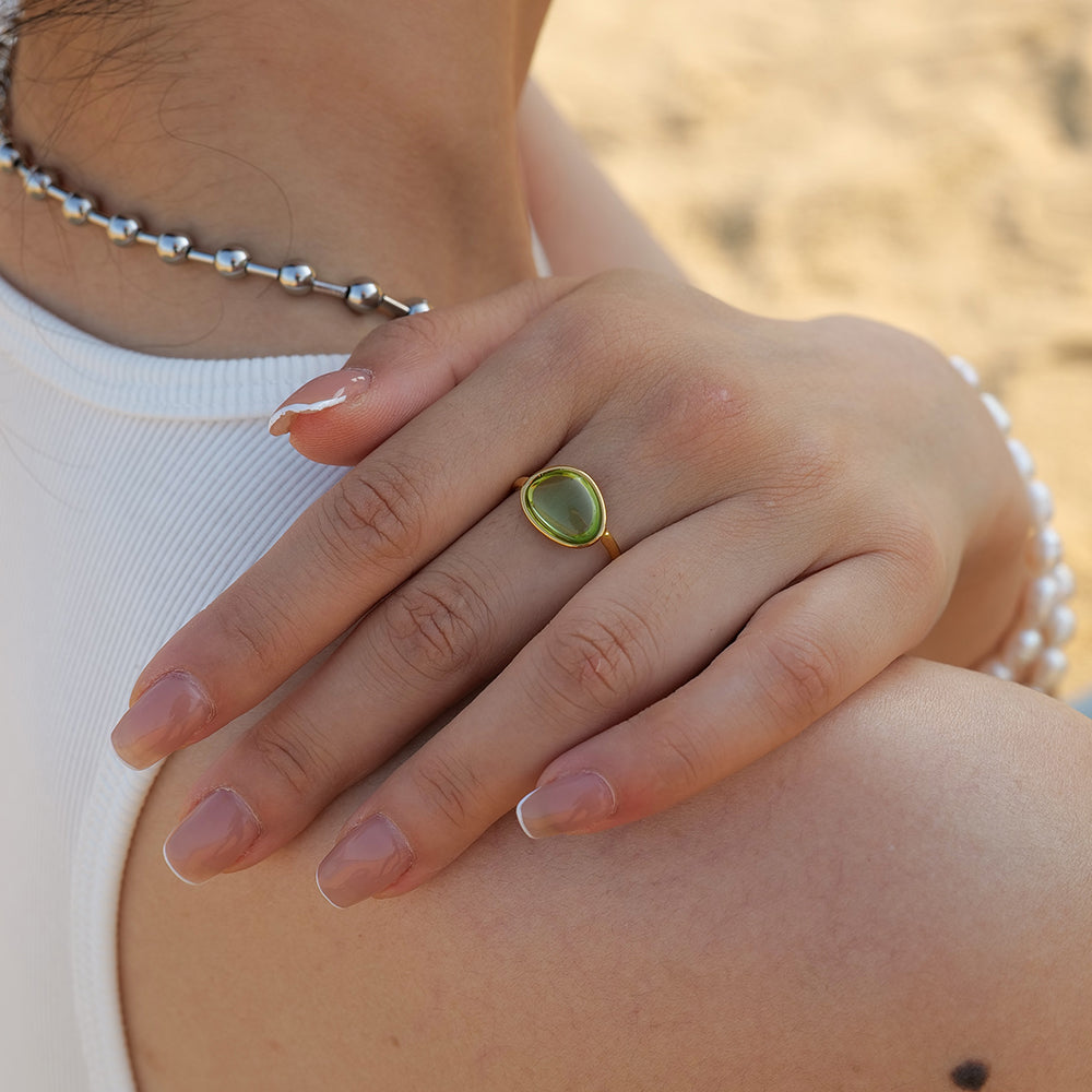 Close-up of a hand wearing a green ring with a blurred background