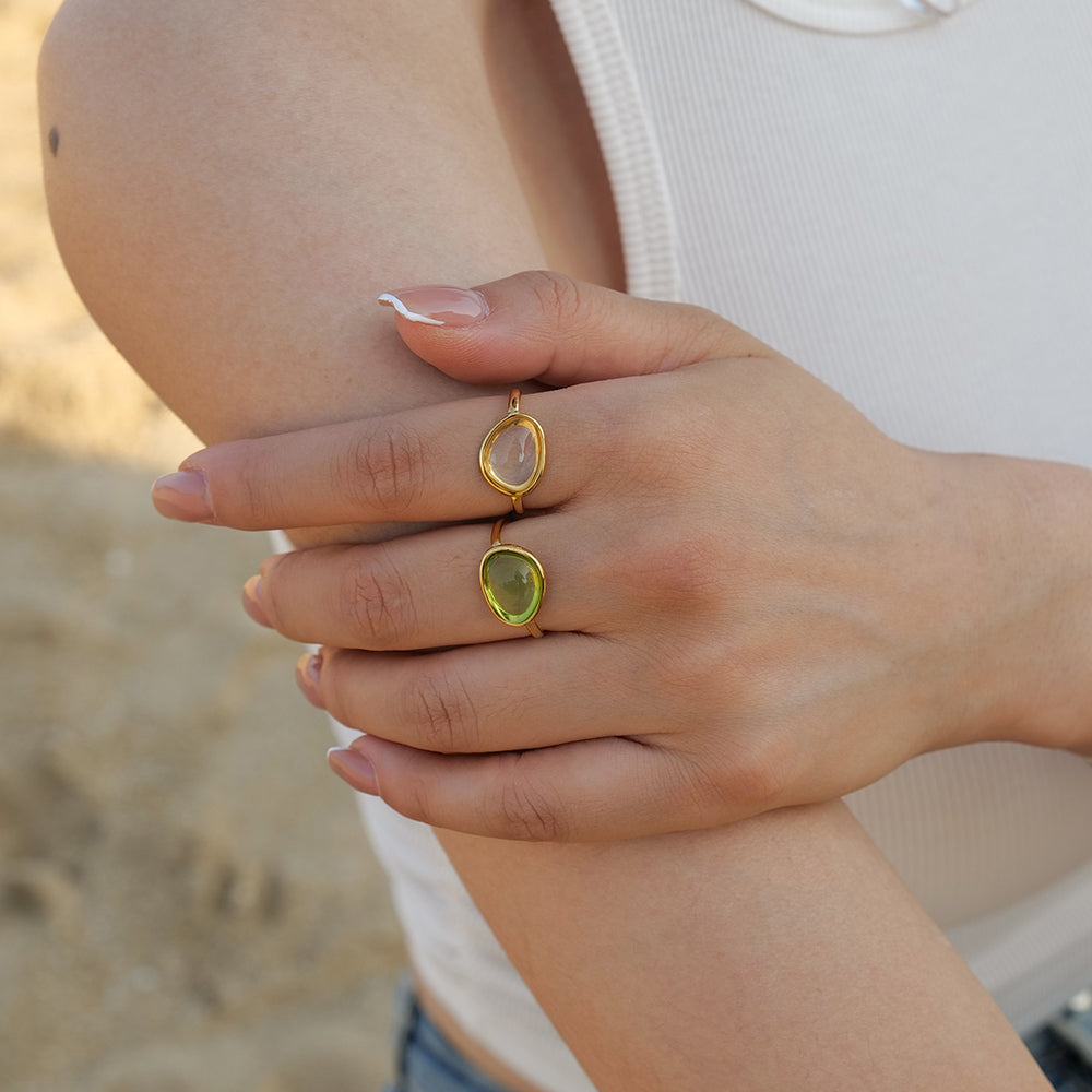 Close-up of a hand wearing two gold rings with gemstones on a blurred beach background