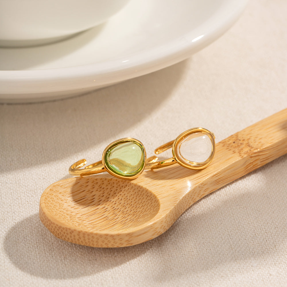 Gold ring with a green gemstone on a wooden spoon with a white plate in the background