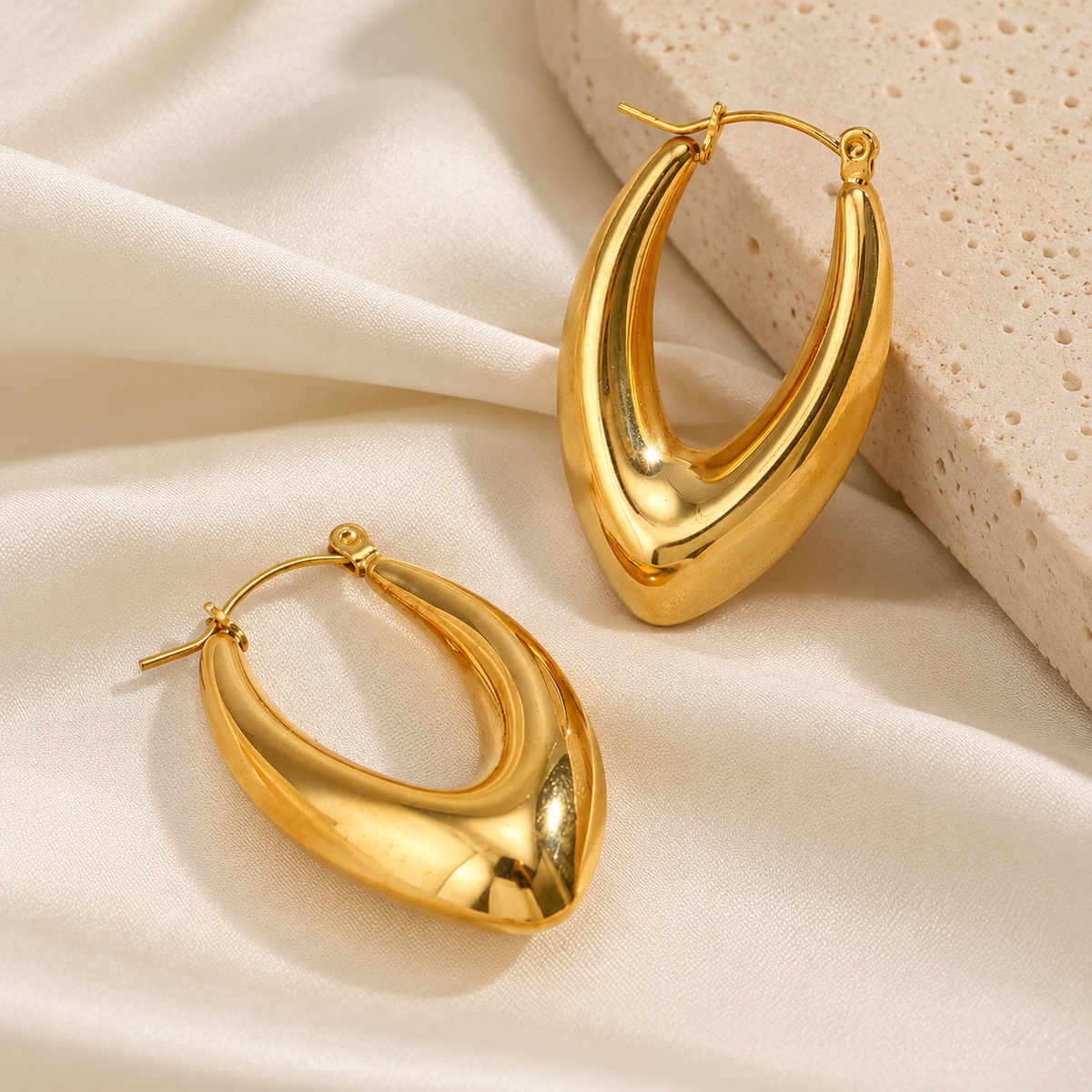 Pair of chunky gold hoop earrings with a sculptural teardrop shape, pointed bottom, polished finish, and hinged closures.