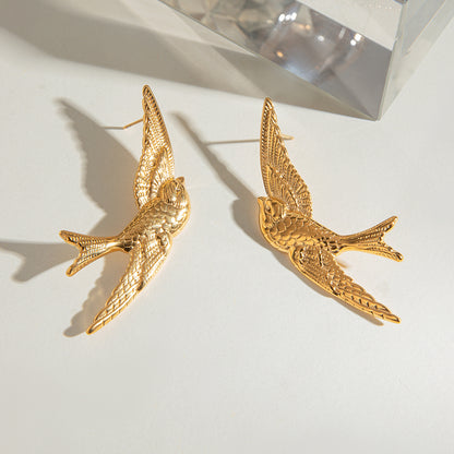 Gold bird-shaped earrings on a light background
