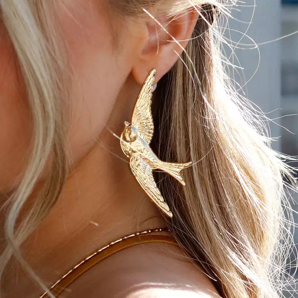 Gold bird-shaped earring worn by a person with blonde hair.
