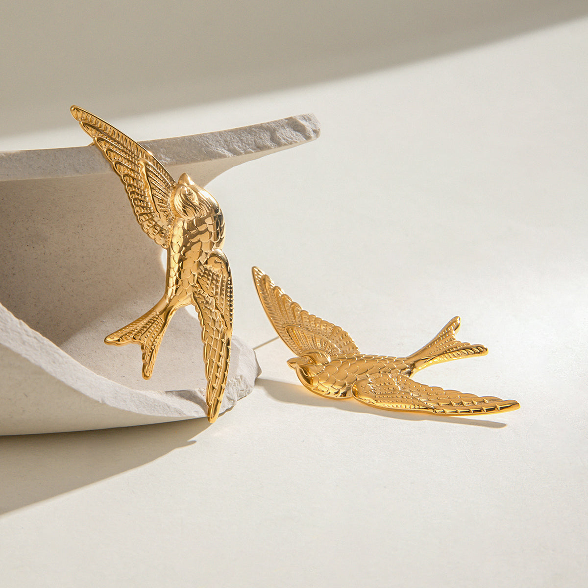 Gold bird-shaped earrings on a light background