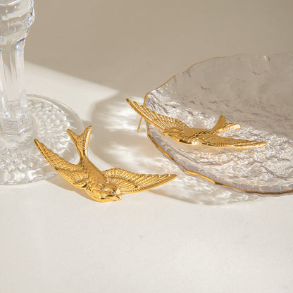 Gold bird-shaped statement earrings on a textured surface