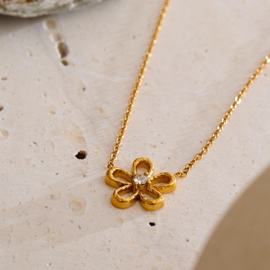 Gold flower-shaped necklace with a diamond on a beige surface