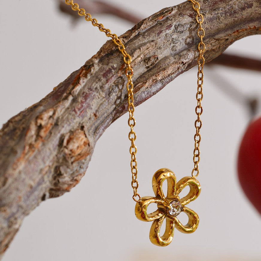 Gold stainless steel flower-shaped necklace hanging on a branch with a blurred background
