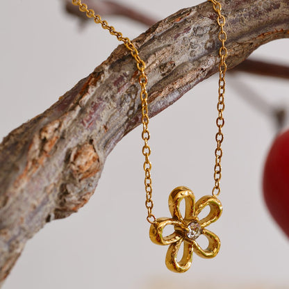 Gold stainless steel flower-shaped necklace hanging on a branch with a blurred background