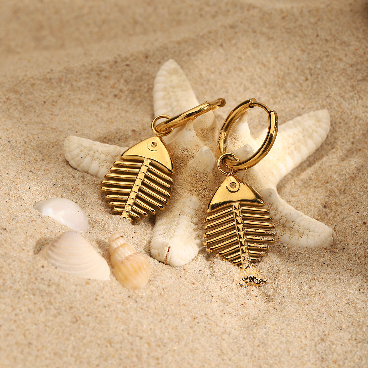 Gold fish-shaped earrings on a starfish and sand background