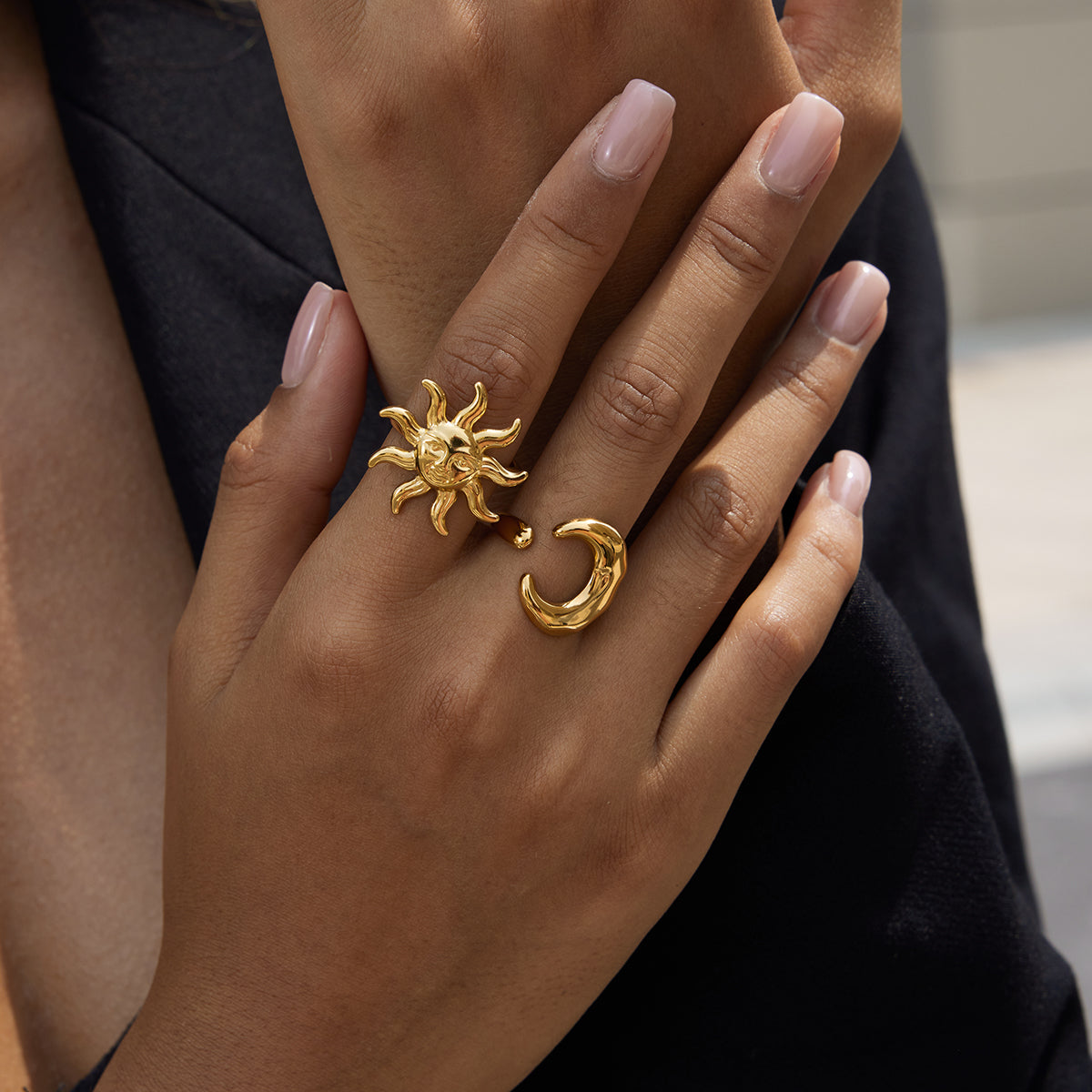 Gold ring with sun and moon design on a hand against a blurred background