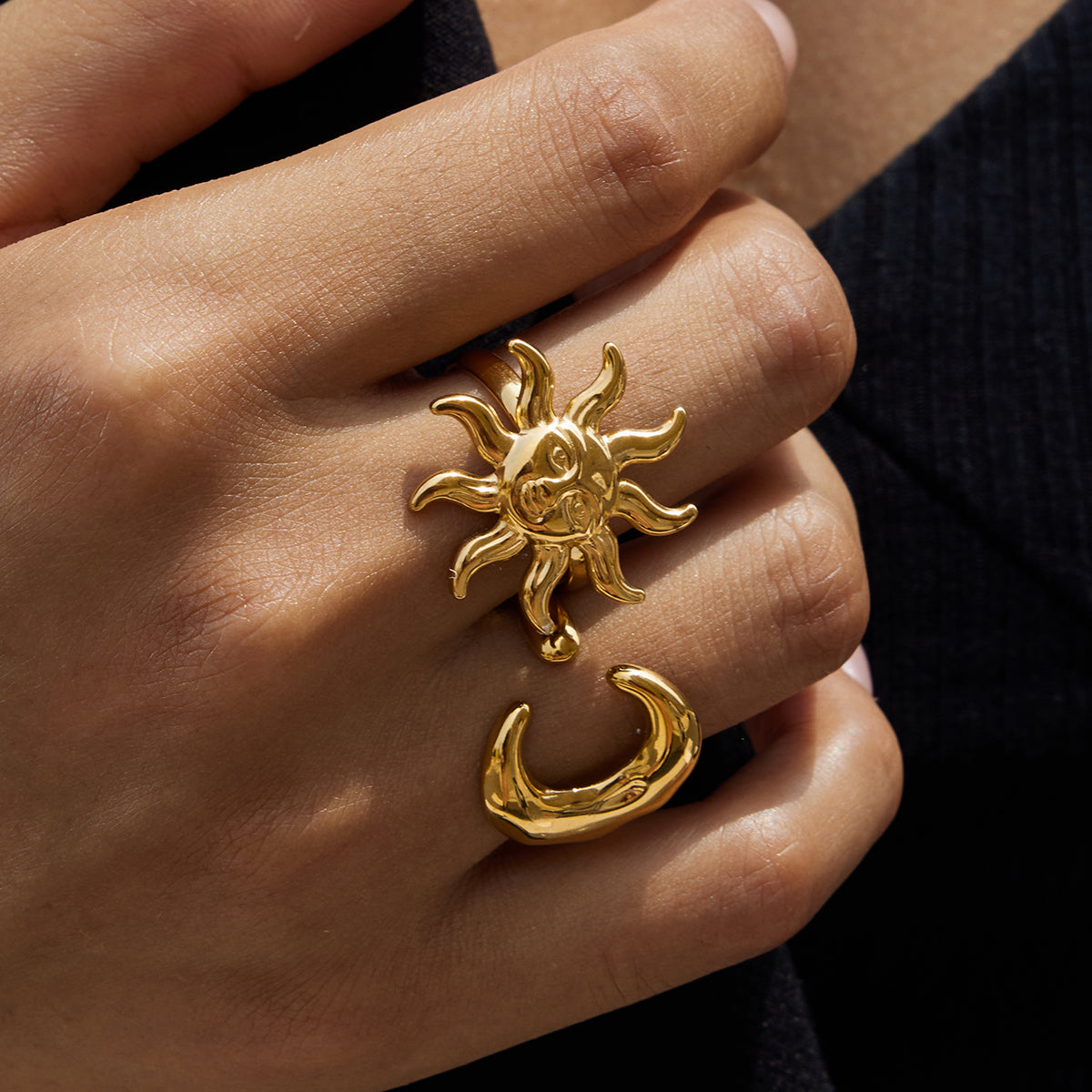 Gold sun and moon ring set on a hand against a dark background