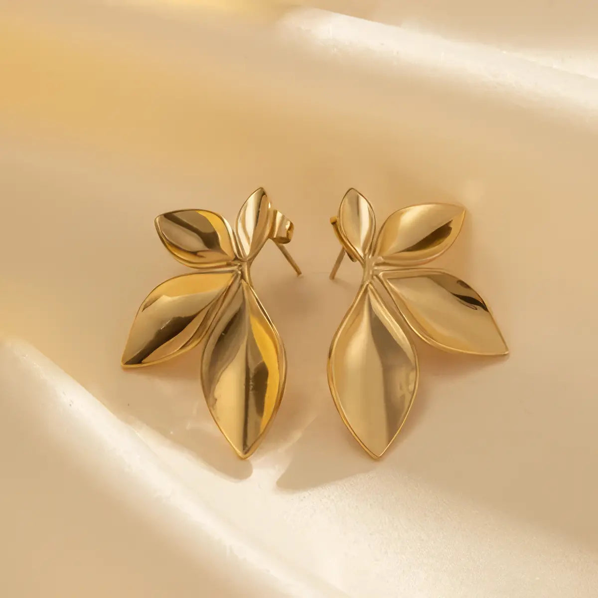 Gold leaf-shaped earrings on a beige background