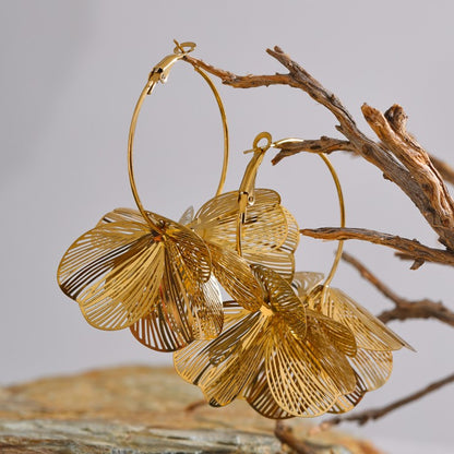 Gold flower earrings on a branch with a neutral background