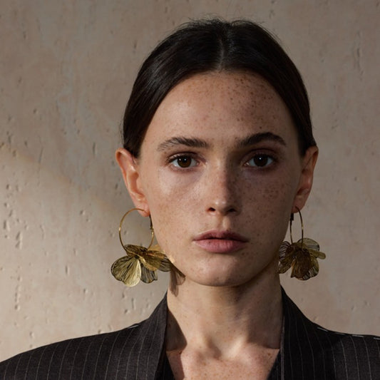 Woman wearing large gold stainless steel hoop earrings against a neutral background
