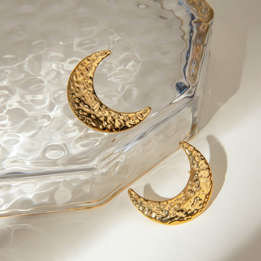 Gold crescent moon earrings on a textured glass surface