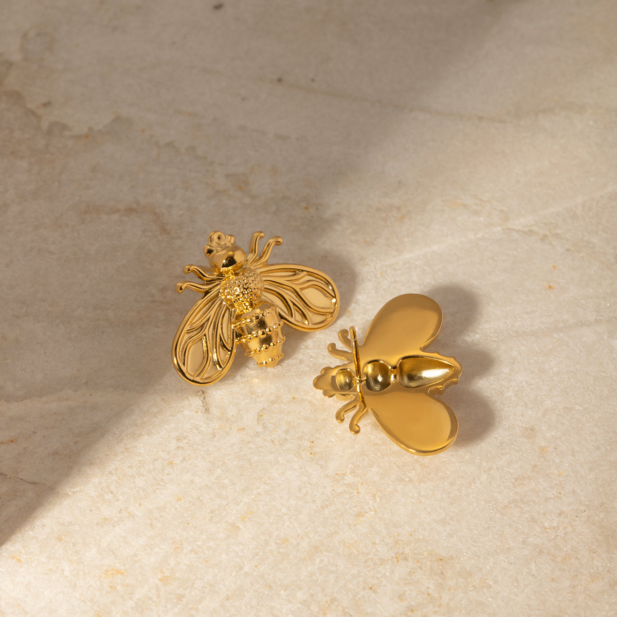 Cute gold bee-shaped earrings on a textured beige surface