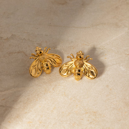 Gold bee-shaped earrings on a beige stone surface