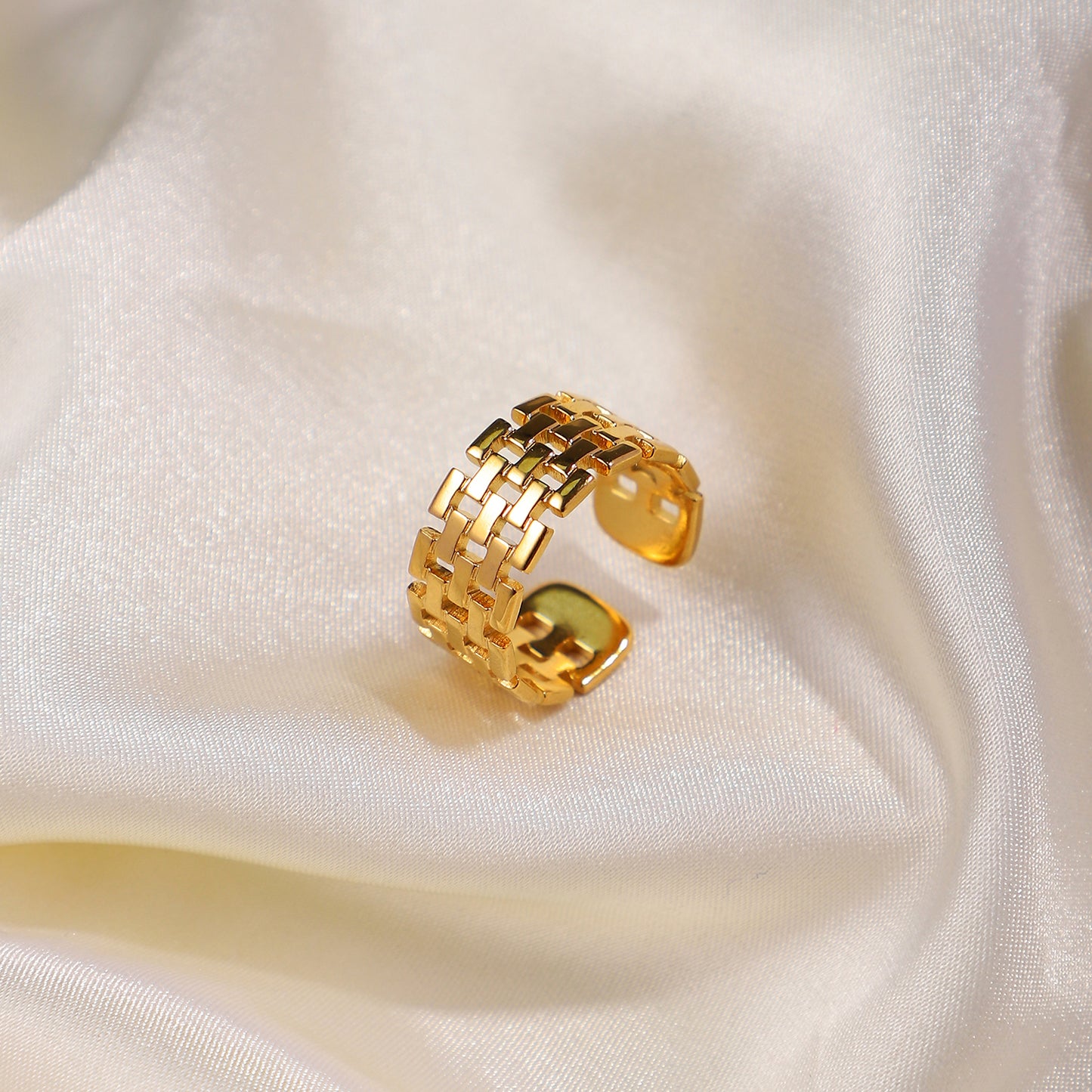 Gold ring with a woven design on a white fabric background