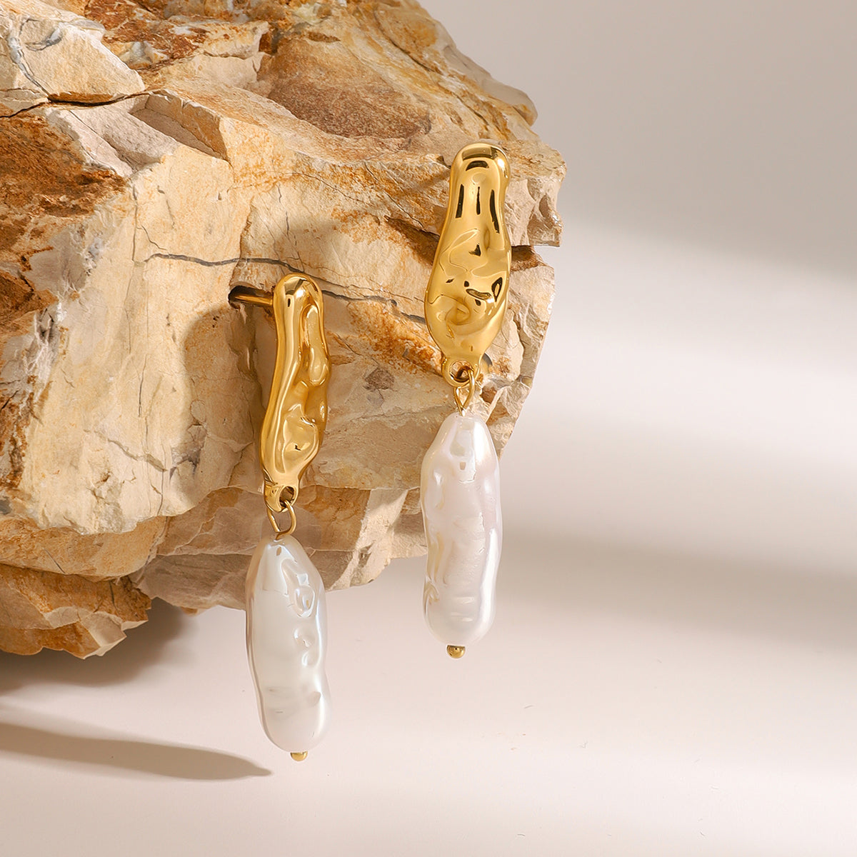 Elegant gold earrings with pearl drops on a stone surface