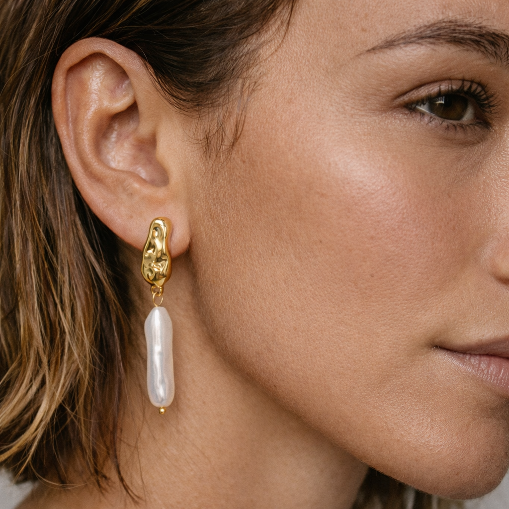 Close-up of a woman wearing a gold earring with a pearl drop.